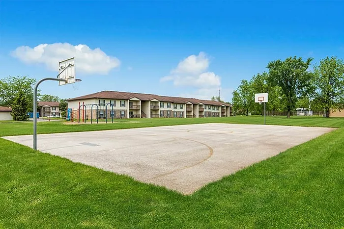 Inviting outdoor basketball court surrounded by lush greenery and a charming apartment complex, perfect for active living.