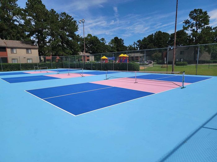 Vibrant blue and pink outdoor tennis and pickleball courts surrounded by lush greenery, offering a lively recreational space in a picturesque setting.