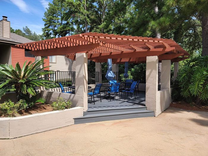 Charming outdoor patio with a wooden pergola and stylish seating area surrounded by lush greenery.