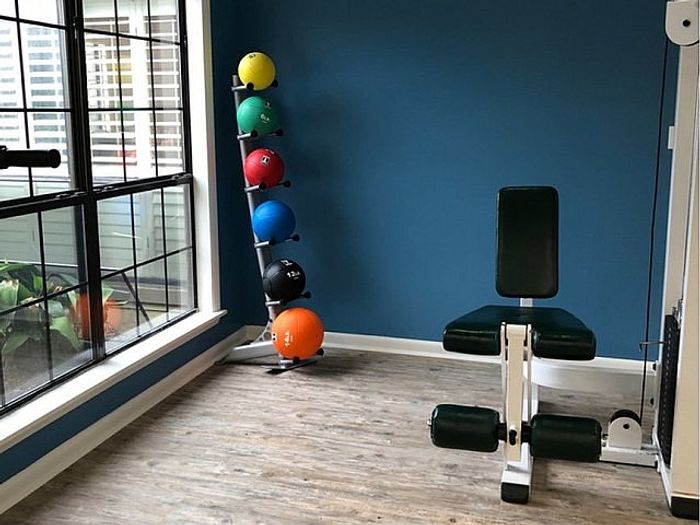 Modern gym corner with vibrant exercise balls neatly stacked beside sleek workout equipment, set against a calming blue wall and sunlit windows.