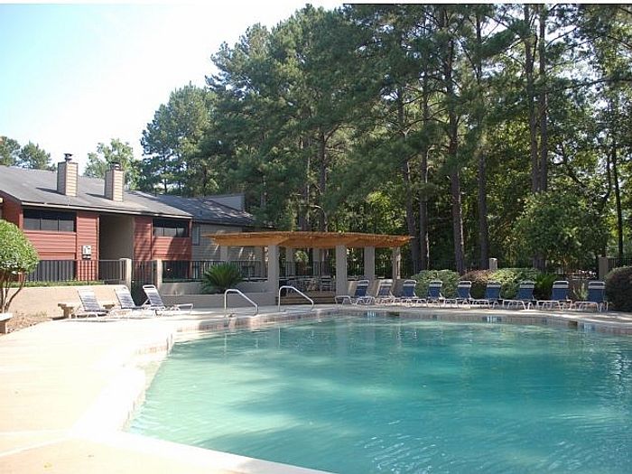 Inviting swimming pool surrounded by lush trees and modern apartment complex with comfortable lounge chairs, perfect for relaxation.
