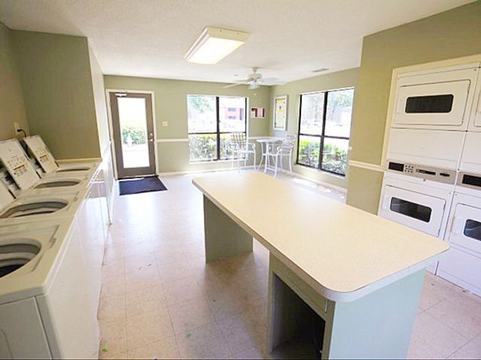 Bright and spacious communal laundry room featuring modern washers, dryers, and a large folding table with expansive windows offering natural light.