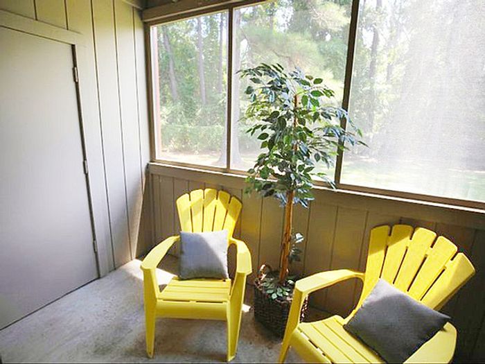 Inviting screened patio with two vibrant yellow chairs, a lush potted plant, and serene woodland views.