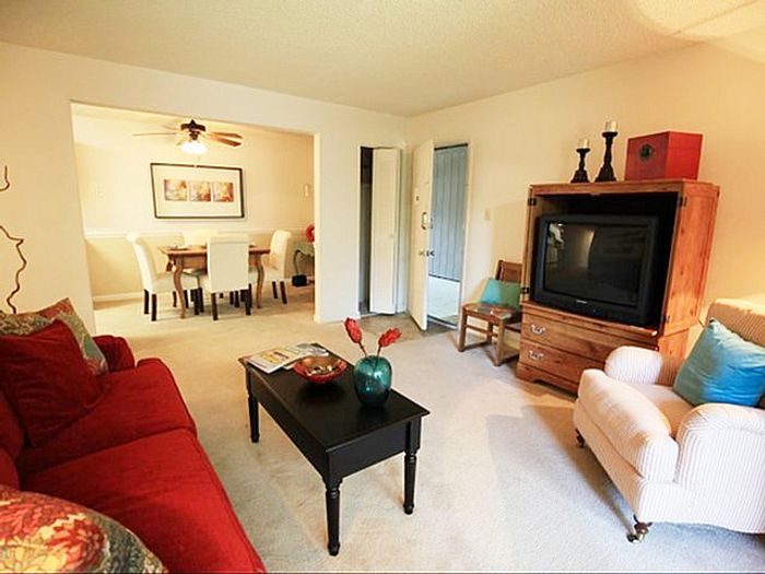 Cozy living room featuring a plush red sofa, elegant decor, and an adjoining light-filled dining area with stylish white chairs.
