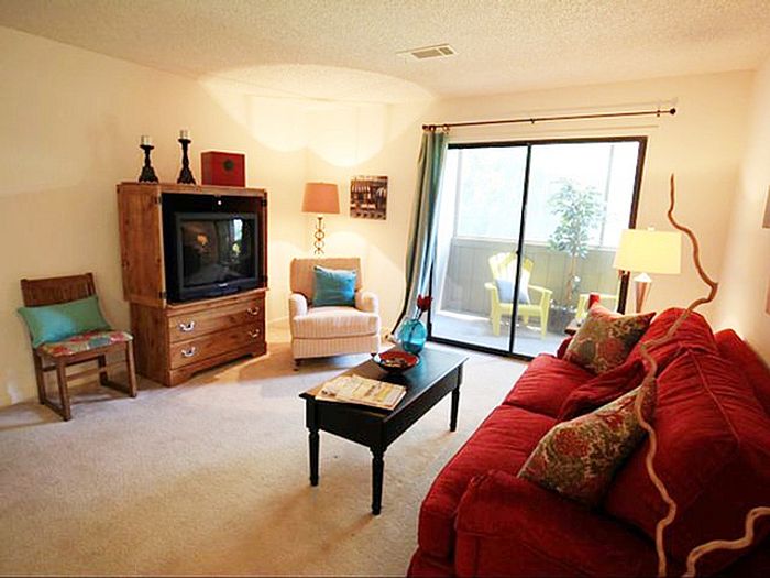 Inviting living room with a plush red sofa, cozy armchair, and elegant TV cabinet; complemented by warm lighting and a serene view of the balcony.