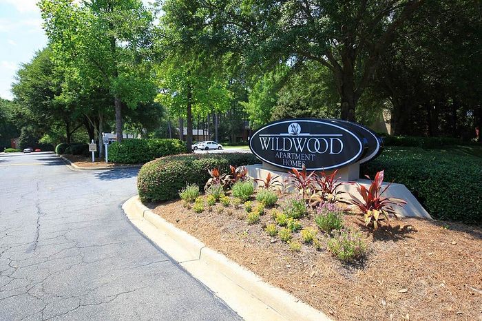 Inviting entrance to Wildwood Apartment Homes surrounded by lush greenery and vibrant landscaping.