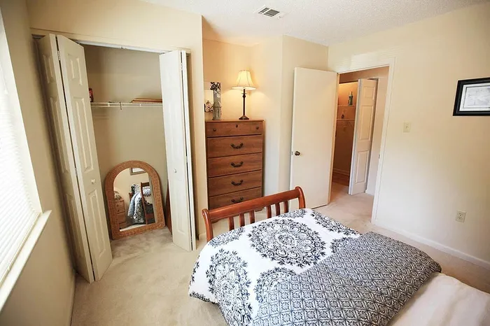 Cozy bedroom with elegant bedding, wooden dresser, open closet, and soft beige walls, creating a warm and inviting atmosphere.