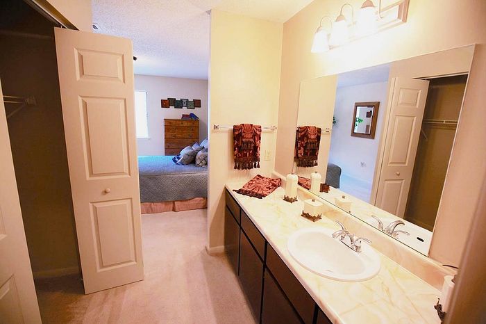 Inviting apartment bathroom with modern fixtures, large vanity mirror, and a view into a cozy, well-furnished bedroom.