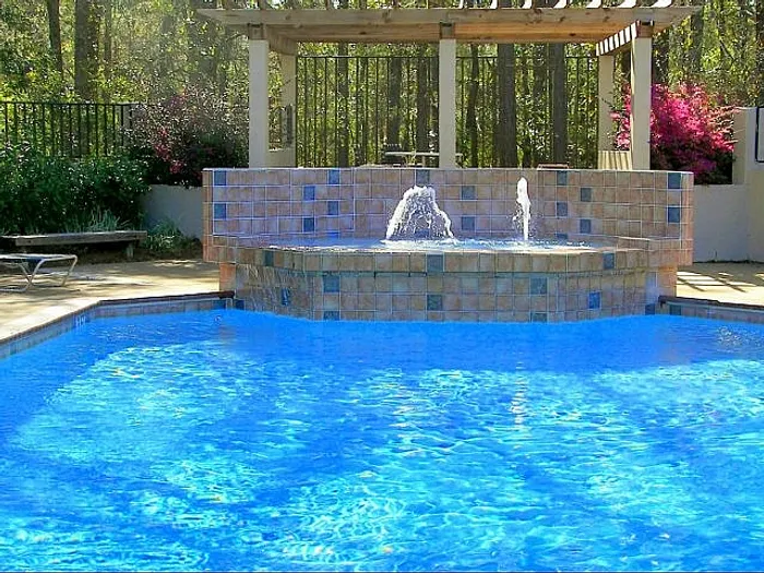 Inviting outdoor pool area with cascading water features surrounded by lush greenery, offering a perfect relaxation retreat.