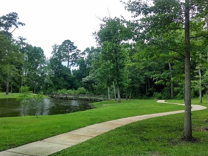 Serene park setting with a winding path alongside a tranquil pond, surrounded by lush green trees.