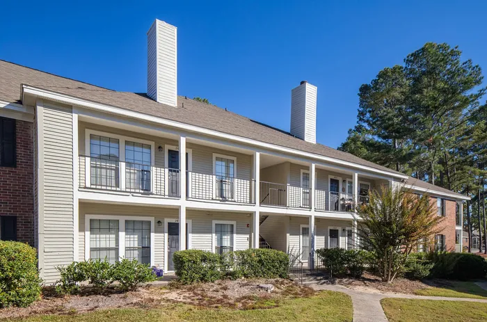 Charming two-story apartment building with balconies and lush greenery, set against a clear blue sky.