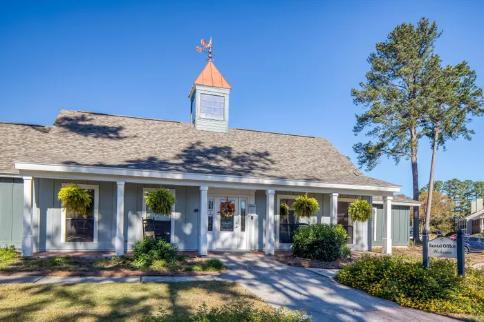 Charming rental office with rustic design, vibrant greenery, and welcoming entryway under a clear blue sky.