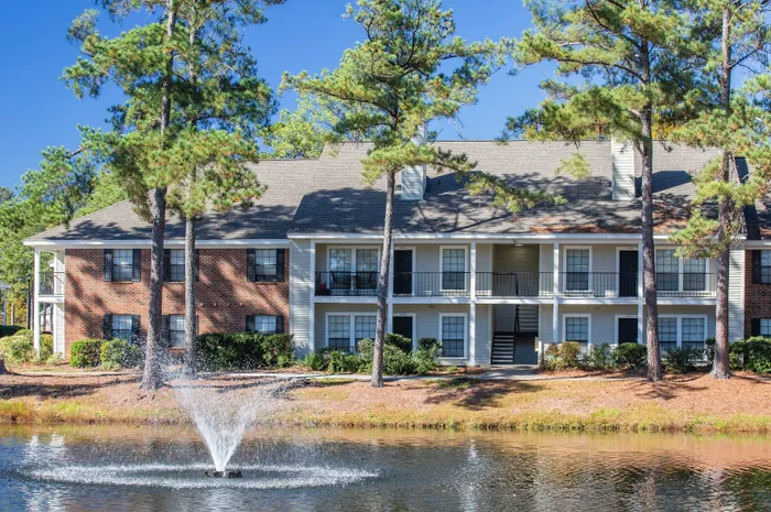 Charming apartment complex with elegant balconies and serene pond view featuring a lovely fountain.
