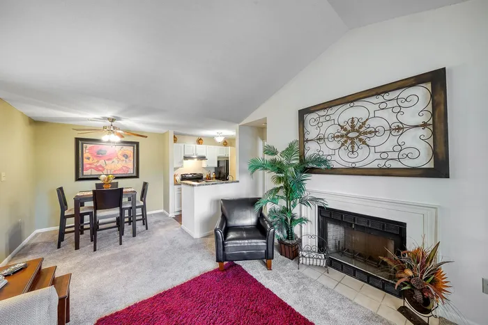 Elegant living room with cozy fireplace, chic armchair, vibrant artwork, and open layout leading to a modern kitchen and dining area.
