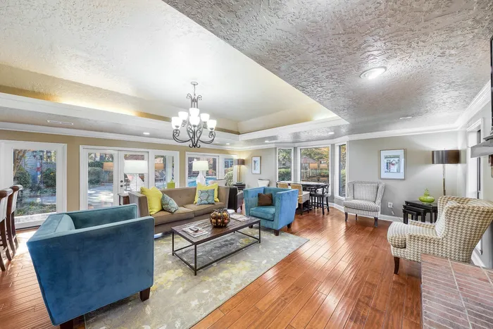 Inviting living room featuring plush blue and beige chairs, chic chandelier, and large windows offering garden views.