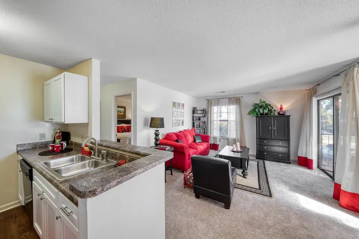Inviting open-plan living area with a modern kitchen, vibrant red sofa, and large window allowing plenty of natural light.