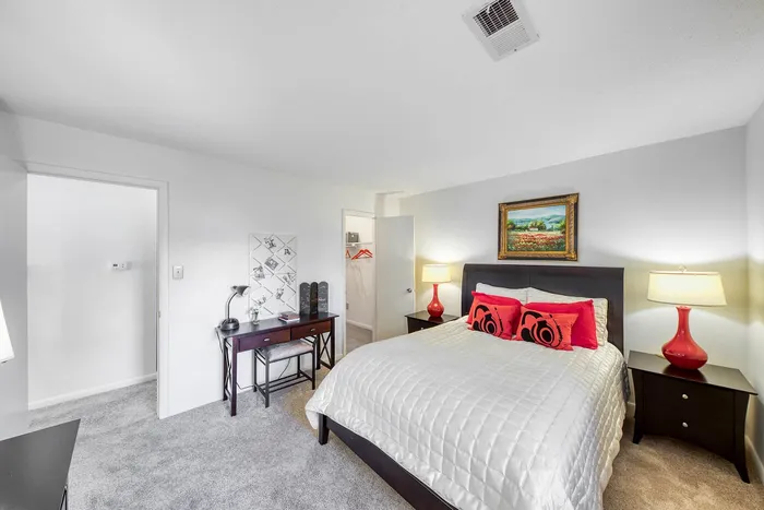 Inviting and stylish bedroom with modern decor, featuring a cozy bed with vibrant red pillows and matching lamps, complemented by a chic work desk and elegant artwork.