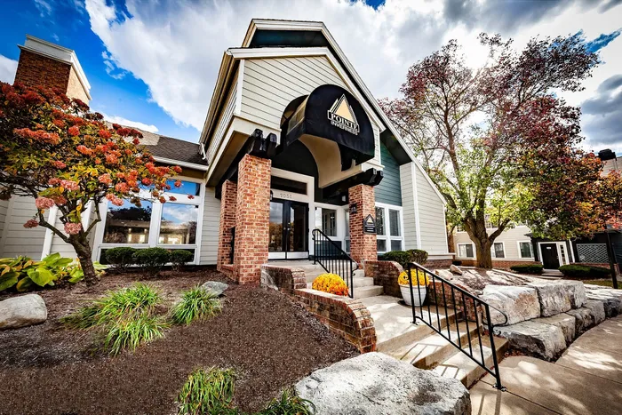 Charming residential entrance with inviting landscaping, scenic brick facade, and vibrant autumn foliage under a bright sky.