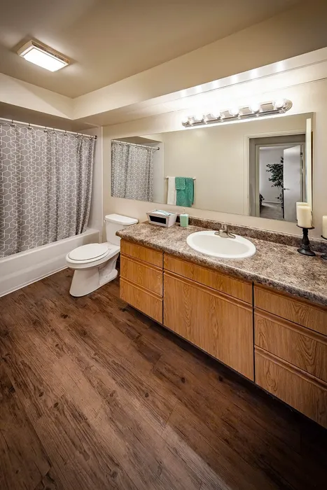 Elegant bathroom featuring a modern vanity with wood cabinetry, sleek countertop, and stylish lighting. Cozy shower-tub combo and chic geometric shower curtain complemented by warm hardwood floors.