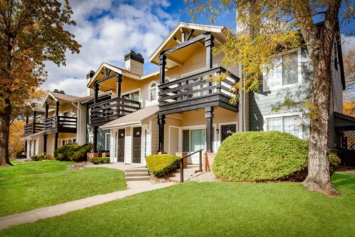 Charming suburban apartments with wooden balconies, surrounded by lush greenery and autumn trees.