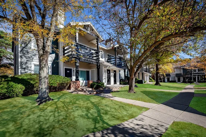 Charming apartment complex with elegant balconies surrounded by lush greenery and scenic pathways under a clear blue sky.