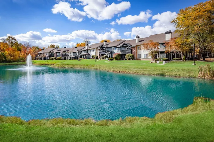 Charming lakeside apartments with beautiful landscaping and a stunning water fountain under a clear blue sky.