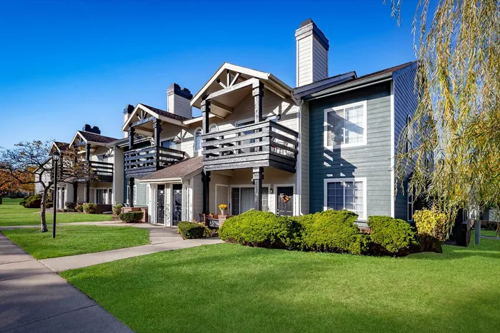 Charming apartment complex with welcoming balconies and lush green lawns under a clear blue sky.