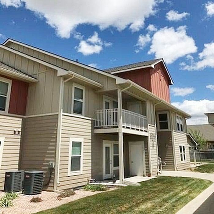 Charming two-story apartment building with modern exterior and private balconies, set against a bright blue sky.