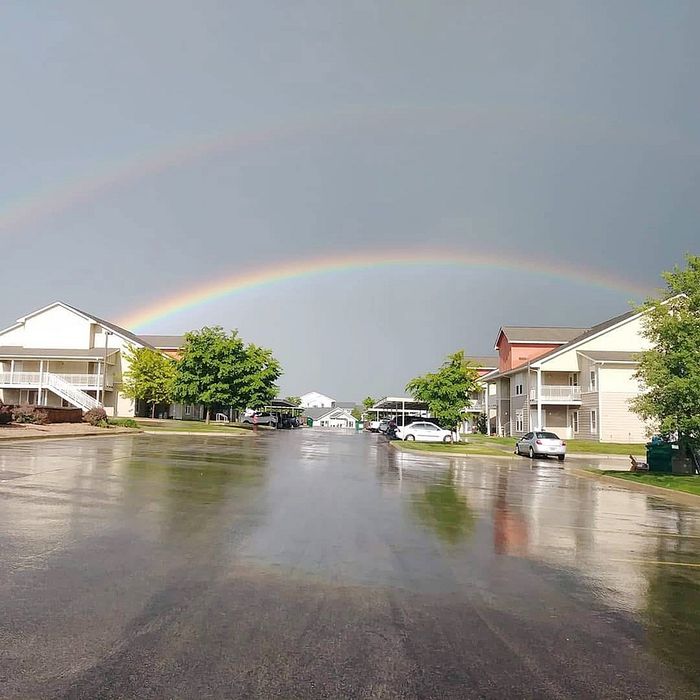 Peaceful residential community street with charming houses and a captivating double rainbow overhead, creating a serene and inviting atmosphere.