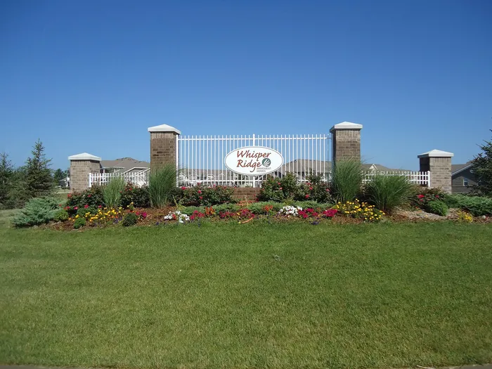 Inviting entrance sign of Whisper Ridge Apartments surrounded by vibrant landscaped gardens and a clear blue sky.