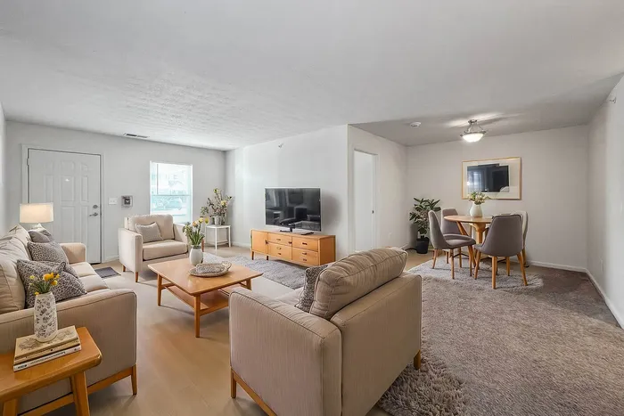 Inviting living room with modern decor, plush sofas, and a flat-screen TV, leading to a cozy dining area with elegant chairs and a stylish table.
