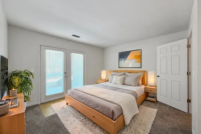Bright and cozy bedroom featuring a plush bed, modern decor, and natural lighting through French doors.