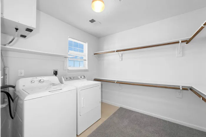 Spacious and bright laundry room featuring modern washer and dryer, ample shelving, and natural light.