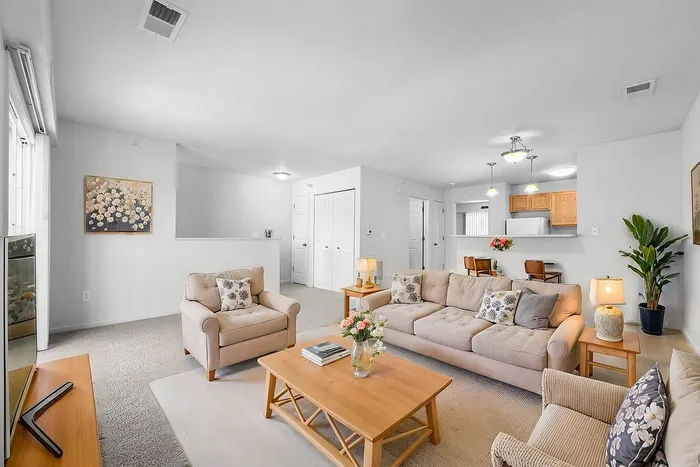 Bright and inviting living room in a modern apartment, featuring cozy beige seating, a stylish wooden coffee table, and a light-filled open concept leading to the kitchen.