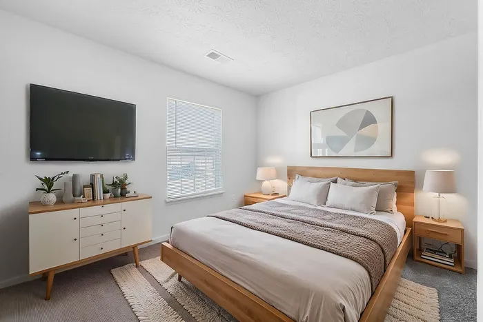 Bright and modern bedroom with a cozy king-size bed, sleek wooden furniture, large TV, and ample natural light from a window, creating a serene and inviting space.
