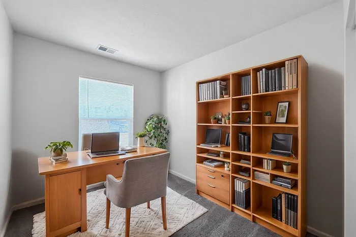 Chic home office with sleek wooden desk, plush chair, and spacious bookcase, flooded with natural light for a perfect work-from-home setting.