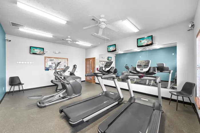 Modern fitness center featuring top-of-the-line treadmills, elliptical machine, and wall-mounted TVs against a stylish blue accent wall.