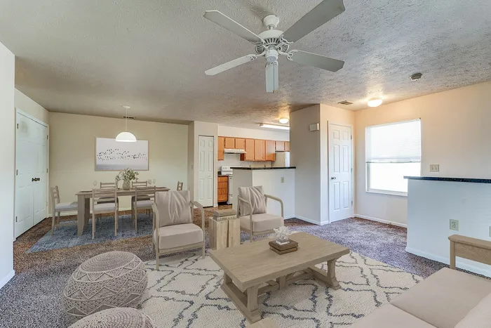 Chic open-concept living and dining area featuring neutral tones, modern furniture, and a ceiling fan, flowing seamlessly into a cozy kitchen with wooden cabinetry.