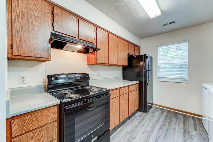 Charming galley kitchen with warm wooden cabinetry, sleek black appliances, and natural light from a bright window.