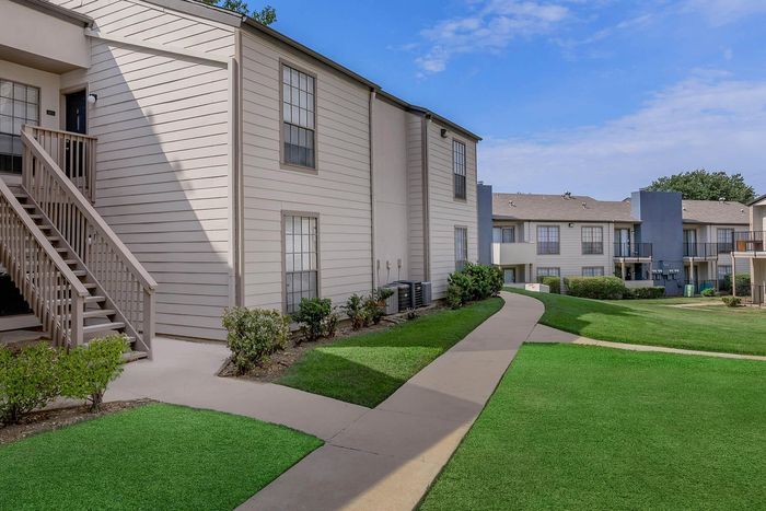 Charming apartment complex with well-maintained landscaping, featuring inviting pathways and modern exteriors under a clear blue sky.