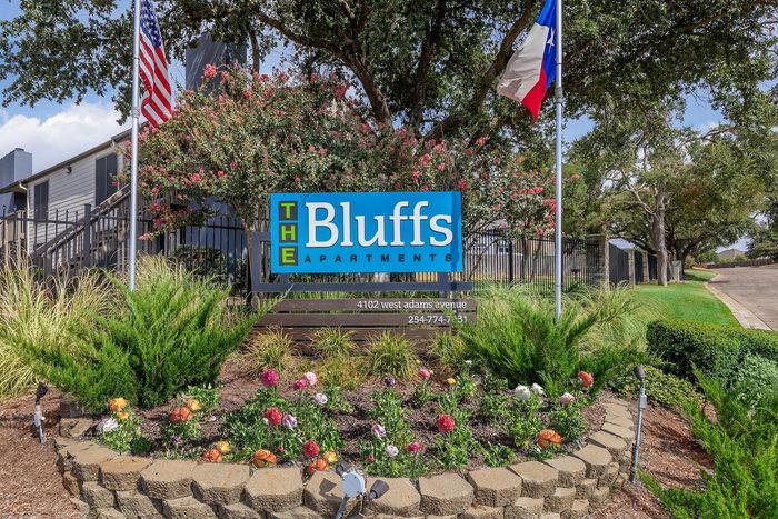 Charming entrance to The Bluffs Apartments with vibrant landscaping and welcoming signage, highlighting a harmonious blend of nature and modern living.