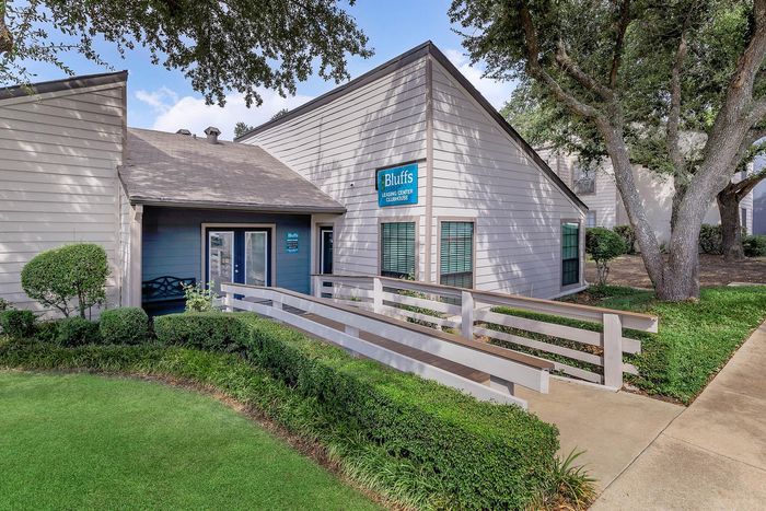 Inviting leasing center exterior with well-maintained greenery and charming walkway at The Bluffs apartment community.