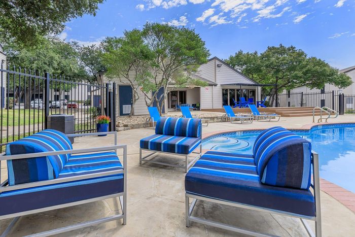 Inviting outdoor area with stylish blue loungers by a sparkling pool, surrounded by lush greenery, ideal for relaxation and leisure.