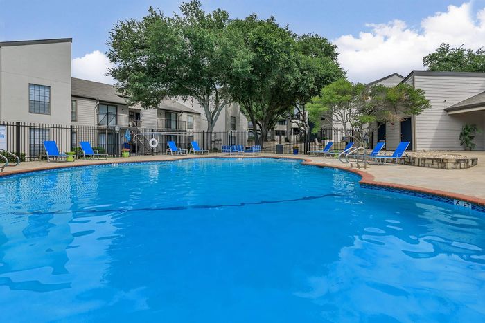 Inviting outdoor swimming pool with vibrant blue lounge chairs and shaded seating in a beautiful apartment community.