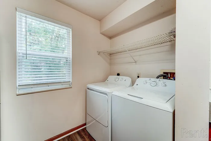 Bright laundry room featuring modern washer and dryer, with a large window providing natural light and a convenient overhead shelf for storage.