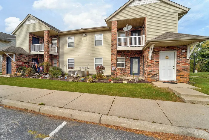 Charming two-story apartment building with brick accents, featuring balconies and landscaped garden beds, perfect for a warm and inviting home.