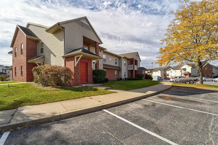 Charming two-story brick apartment building with vibrant autumn foliage, ample parking, and well-maintained lawns.