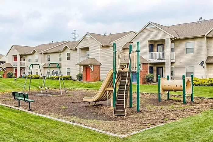 Inviting apartment complex with family-friendly playground, featuring swings and slide, nestled in a lush green landscape.