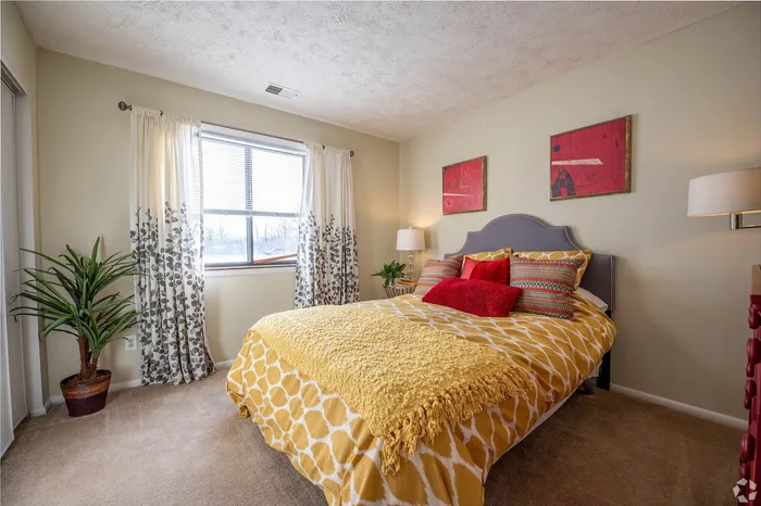 Bright and cozy bedroom featuring a stylish bed with vibrant pillows, large window with elegant curtains, and tasteful wall art.