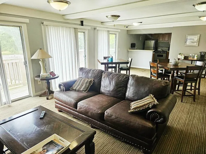 Inviting open-concept living area with a leather sofa, elegant dining table, and modern kitchen, flooded with natural light from expansive sliding glass doors.